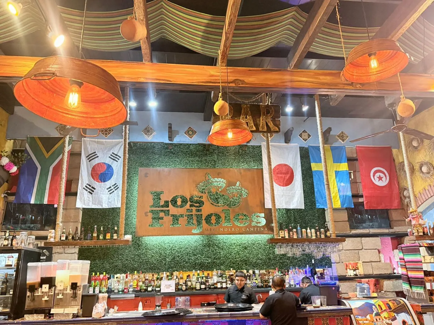 Barra de la cantina de Los Frijoles con el logo en muro verde y banderas de varios países