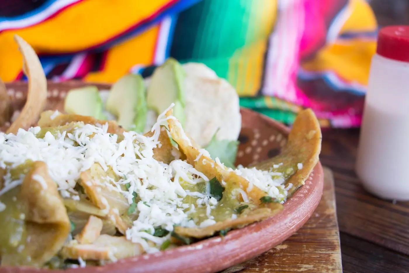 Chilaquiles verdes con queso rallado y aguacate en plato de barro
