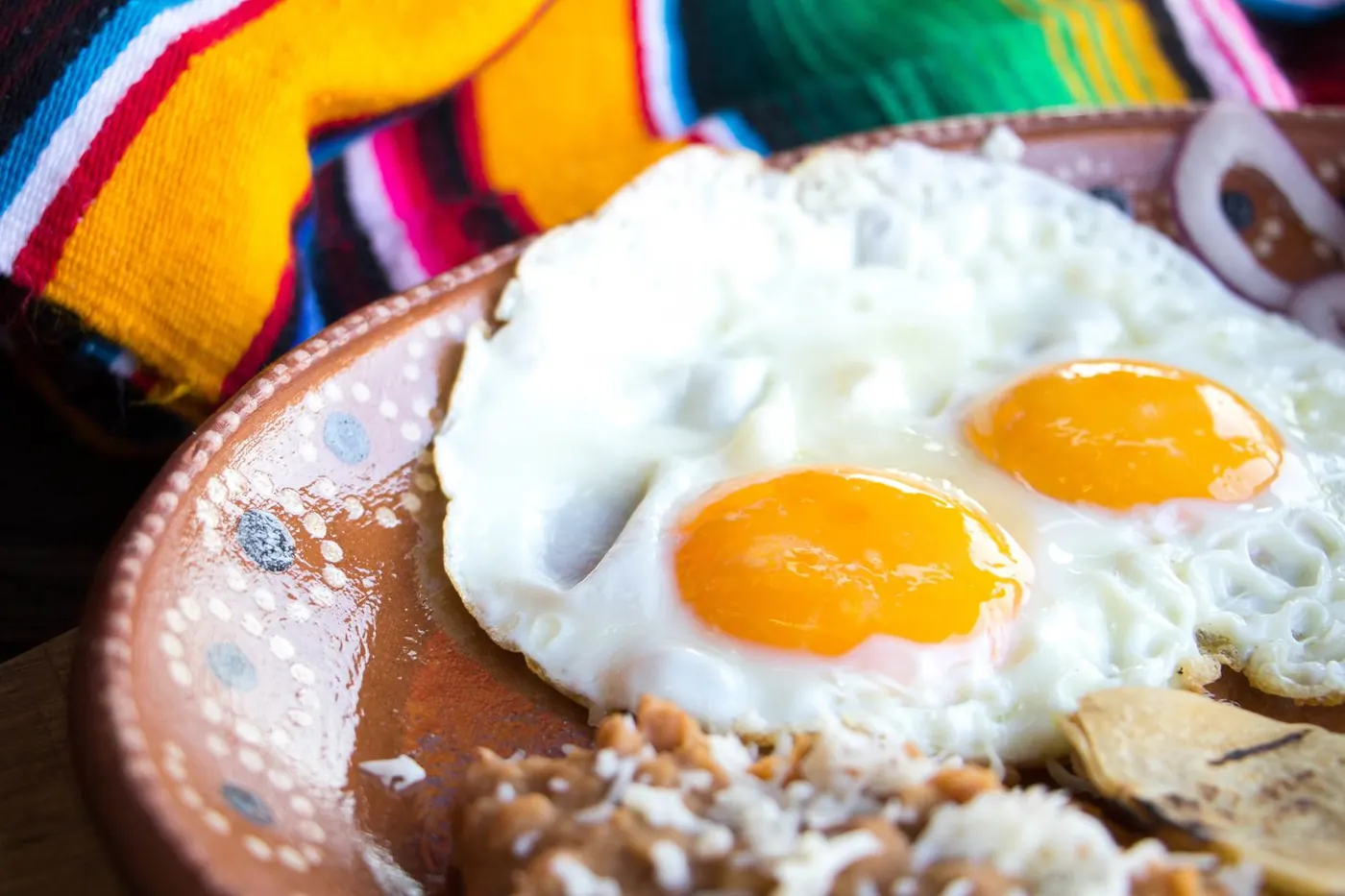 Huevos estrellados con frijoles refritos y queso en plato de barro