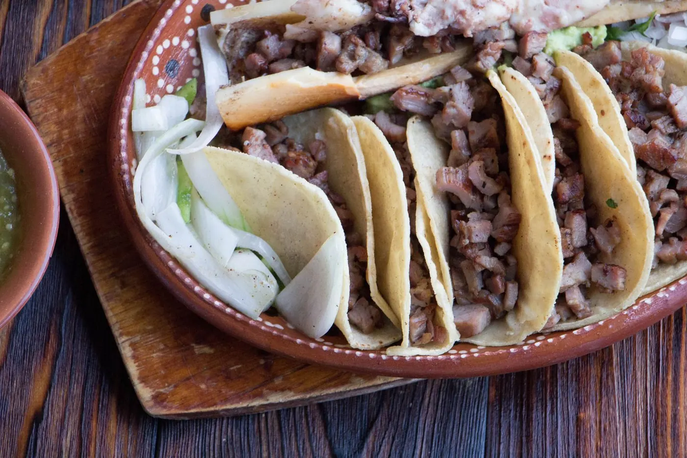 Tacos de carnitas estilo mexicano en plato de barro con cebolla y guacamole